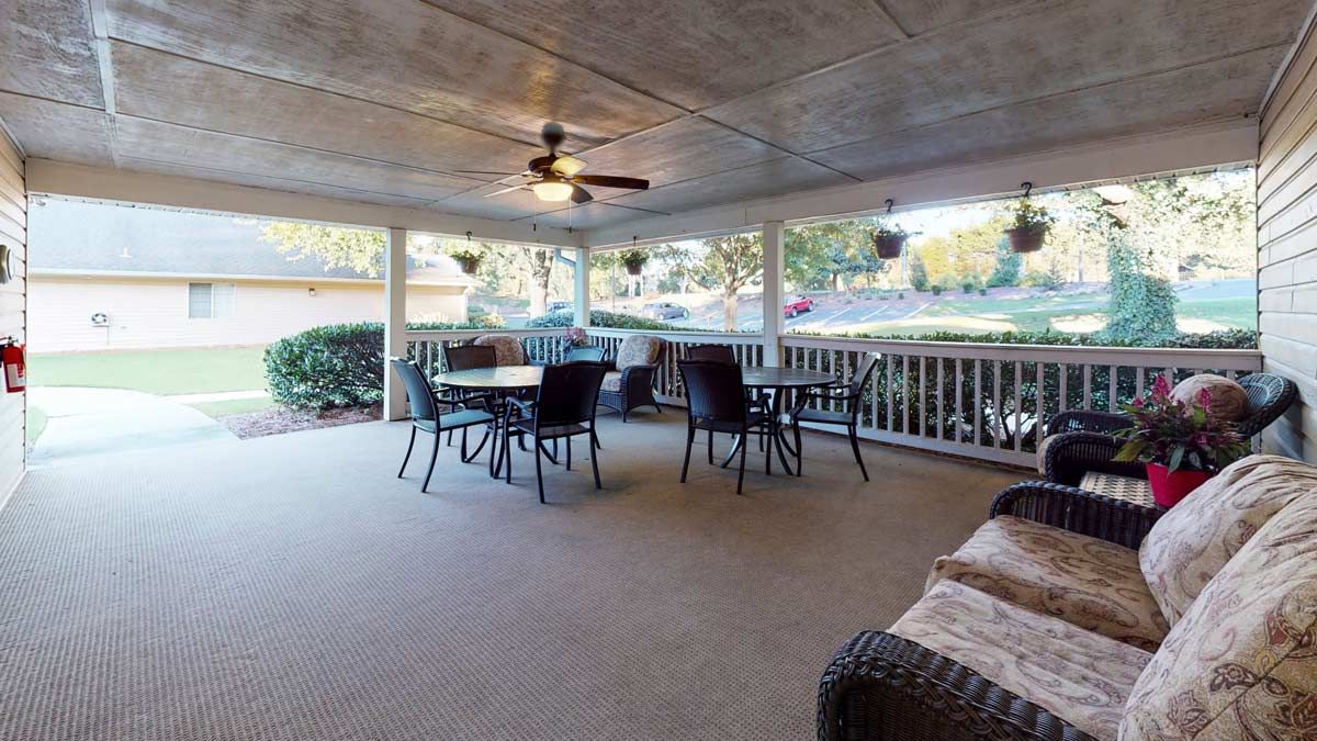 A cozy covered patio featuring outdoor seating with tables and chairs, a ceiling fan, and hanging plants.
