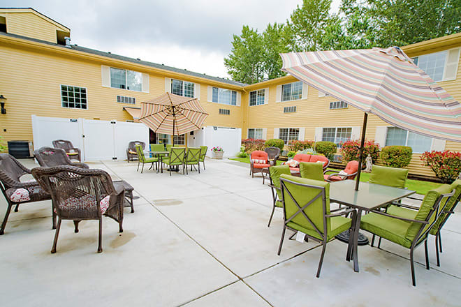 A spacious outdoor patio area with tables, chairs, and umbrellas, surrounded by a two-story yellow building.