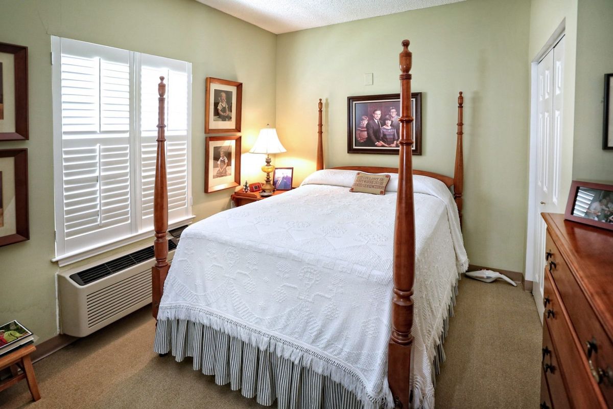 A cozy bedroom featuring a four-poster bed with white bedding, complemented by a bedside lamp and framed artwork on the walls.