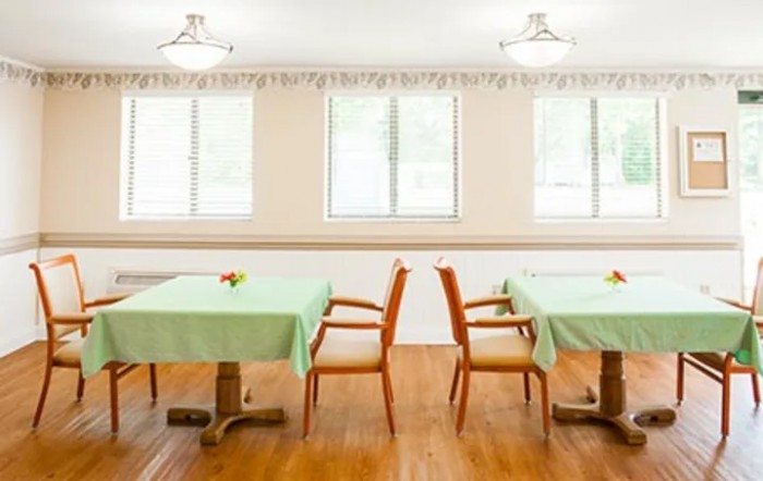 A tidy dining room with tables covered in green tablecloths and wooden chairs.