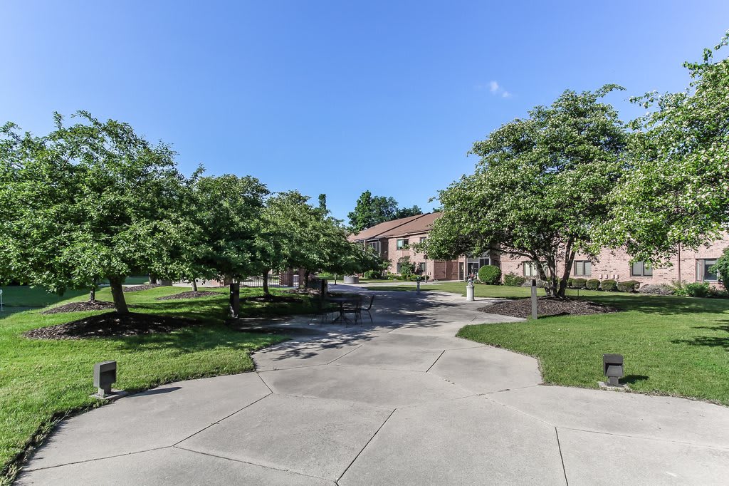 A sunny view of a building surrounded by trees and a sidewalk in a landscaped setting.