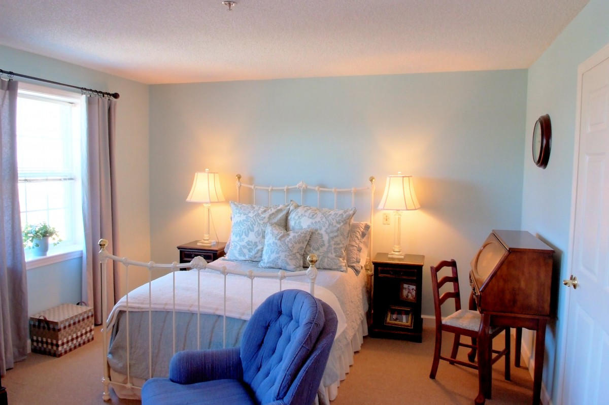 A cozy bedroom with a white metal bed, blue chair, and wooden desk.