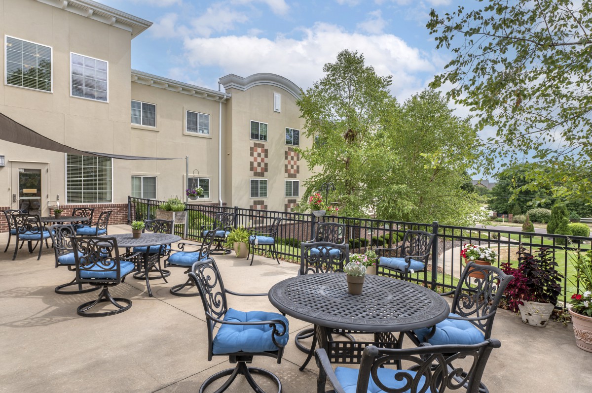 A sunny outdoor patio with tables and chairs, adjacent to a building.