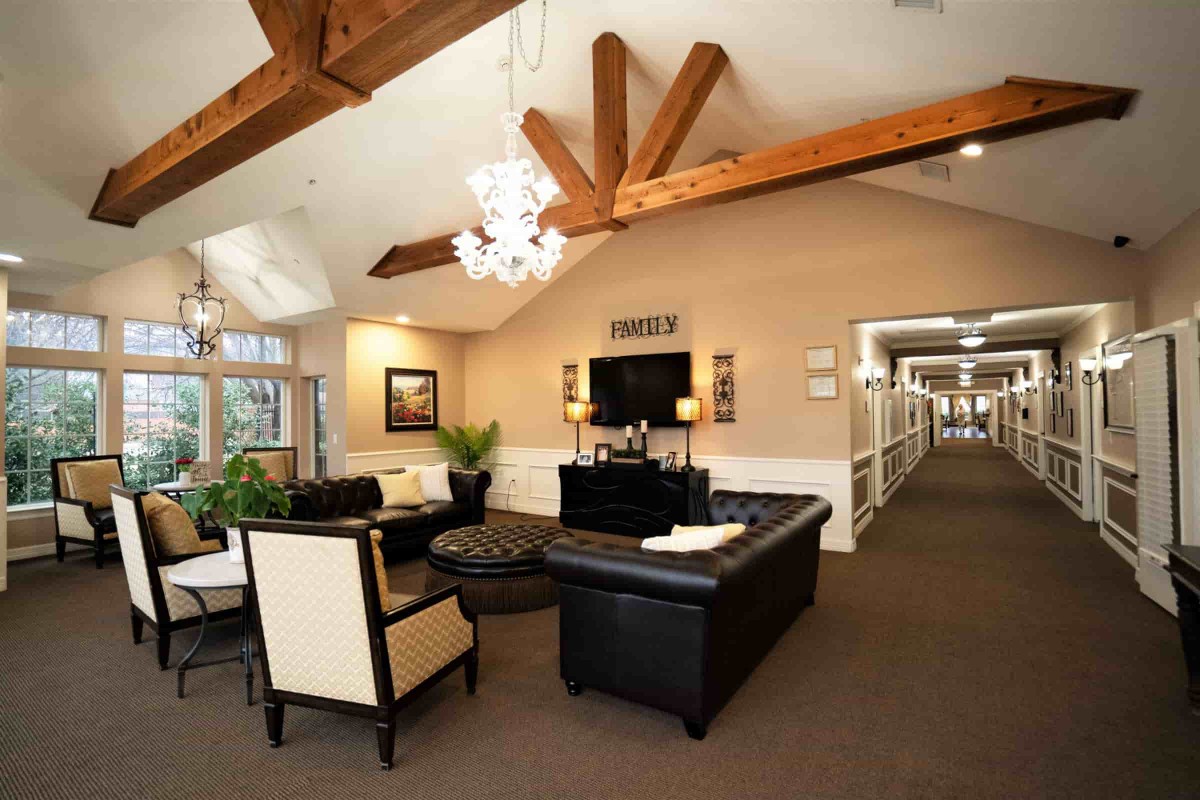 A modern living room with elegant decor, featuring black sofas, a chandelier, and wooden ceiling beams.