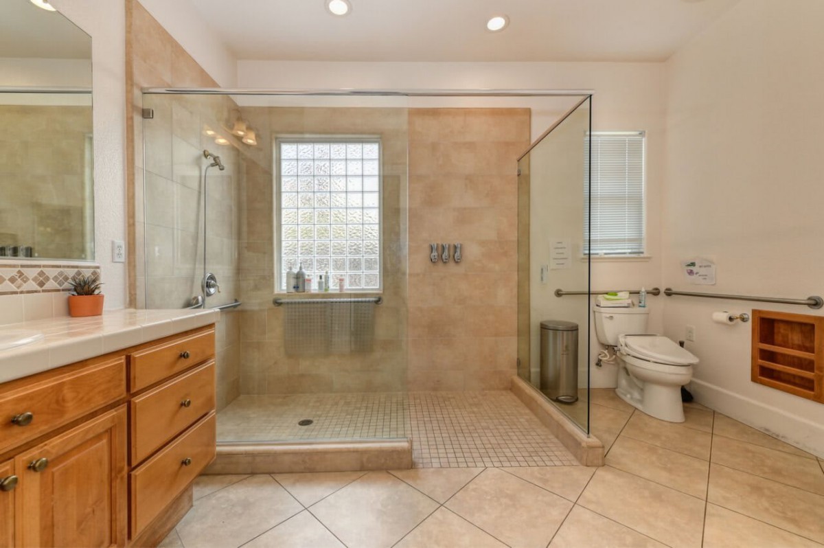 A modern bathroom featuring a glass-enclosed shower, wooden cabinetry, and tiled flooring.