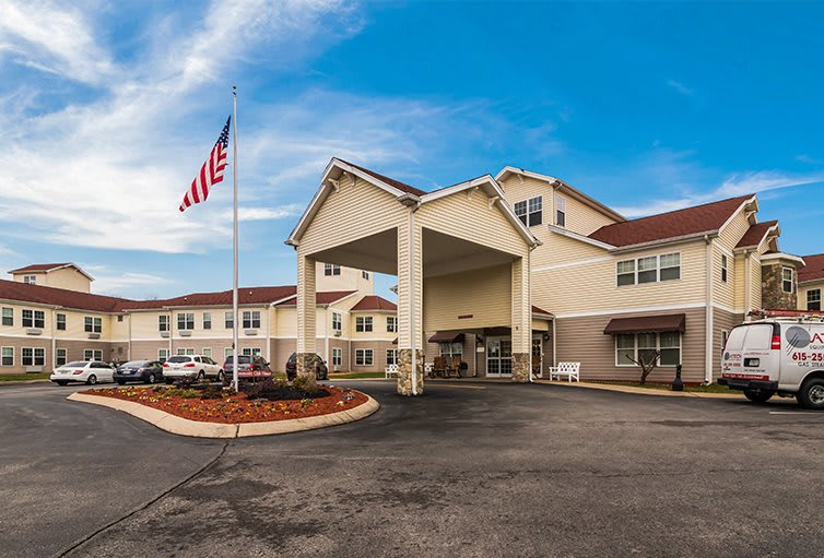 A hotel building with an entrance, parking area, and a flagpole in front.
