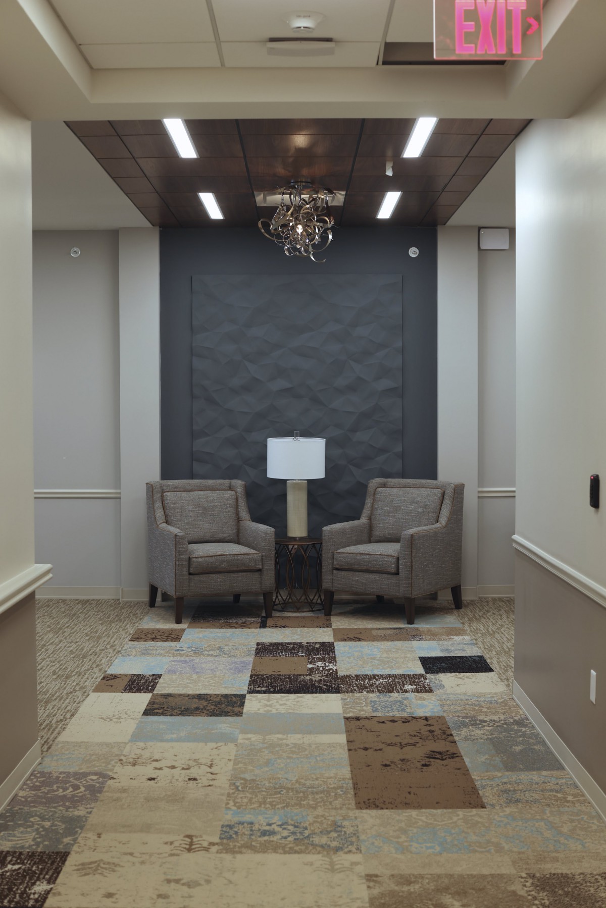 A modern waiting area with two chairs, a central lamp, and a chandelier.