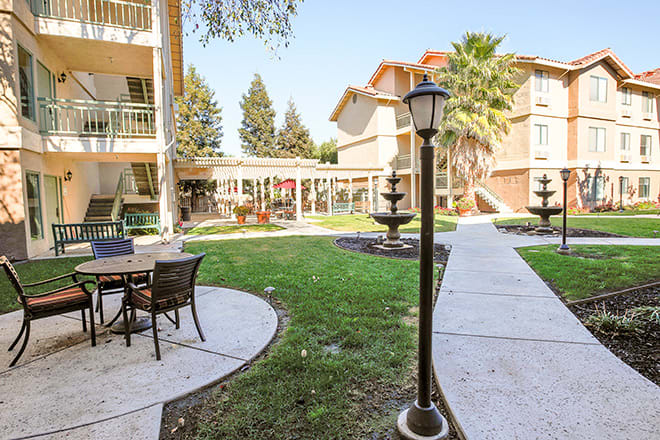 A serene courtyard at an apartment complex, featuring outdoor seating, a fountain, and well-maintained landscaping.
