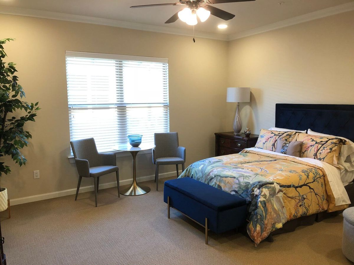 A cozy bedroom featuring a bed with colorful bedding, two chairs with a small table by the window, and a lamp in the corner.