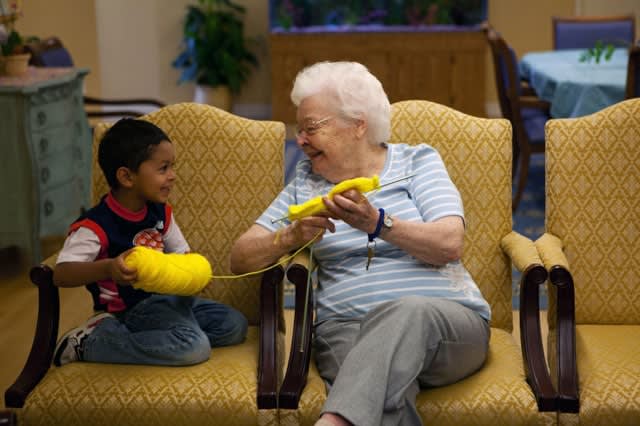 An elderly woman and a young child share a joyful moment while knitting together.