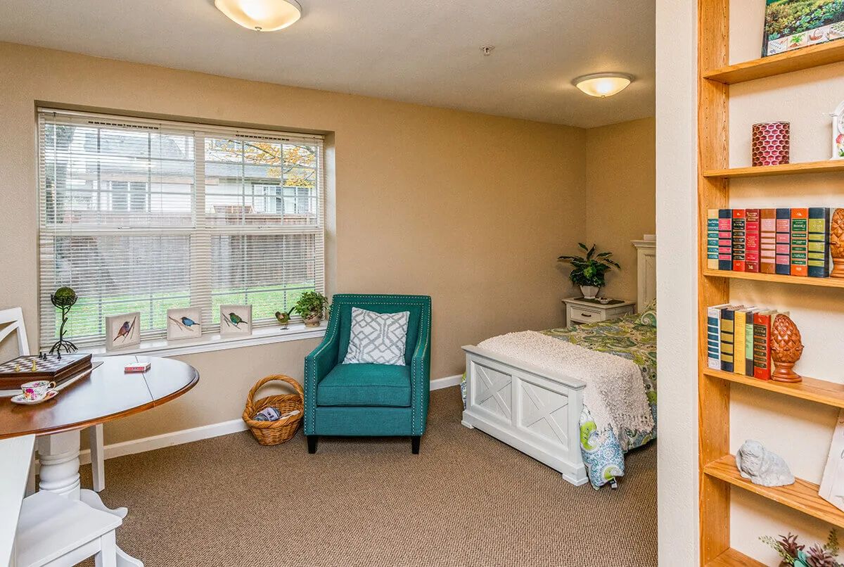 A cozy bedroom interior with a teal armchair and white bed near a window.