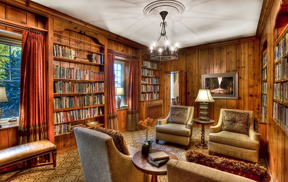 A cozy library with wooden paneling, filled with bookshelves and comfortable seating.