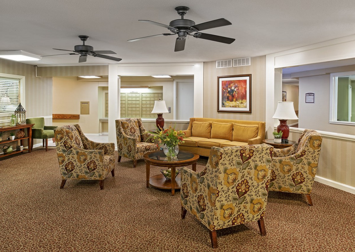A cozy living room with comfortable seating, featuring a sofa, patterned chairs, lamps, and ceiling fans.