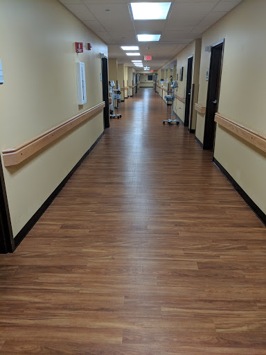A view of a hospital corridor featuring wooden flooring and soft lighting.