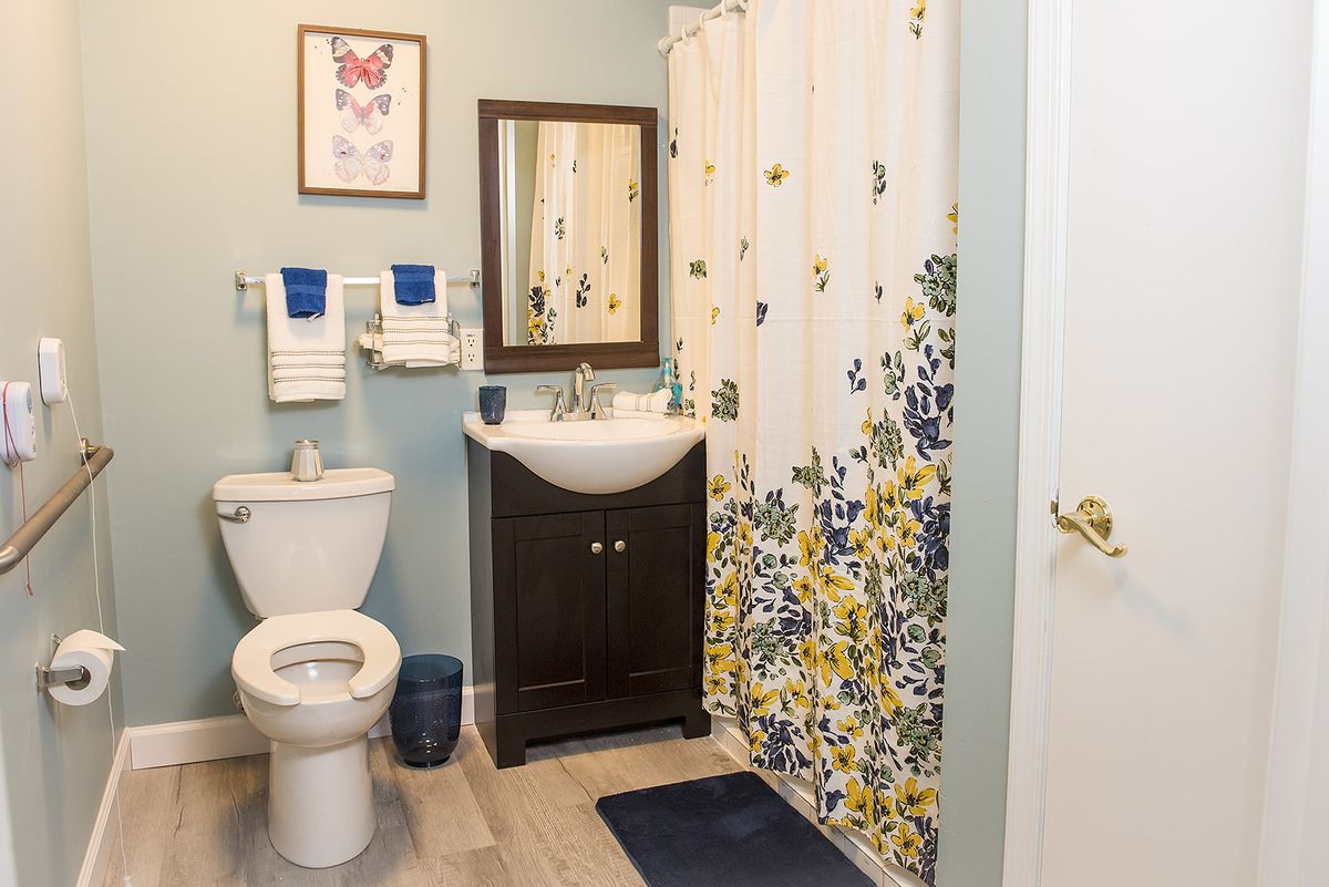 A modern bathroom with a floral shower curtain, wall mirror, and neatly arranged towels.