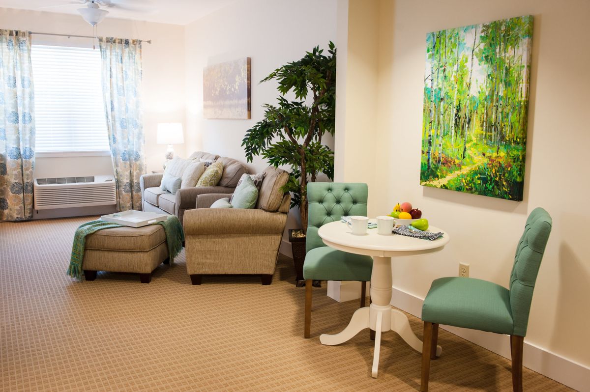 A cozy and well-decorated living room with a sofa set, armchair, a small round table with chairs, and vibrant wall art.