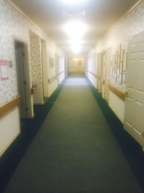 A long, carpeted hallway with multiple doors and bright overhead lighting.