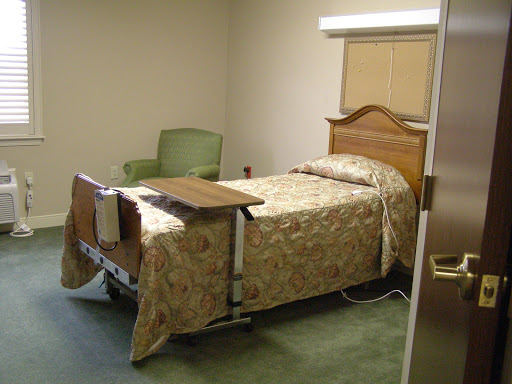 A hospital room featuring a bed with a decorative cover, a bedside table, and a chair.