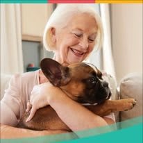 An elderly woman smiling as she lovingly hugs her dog indoors.