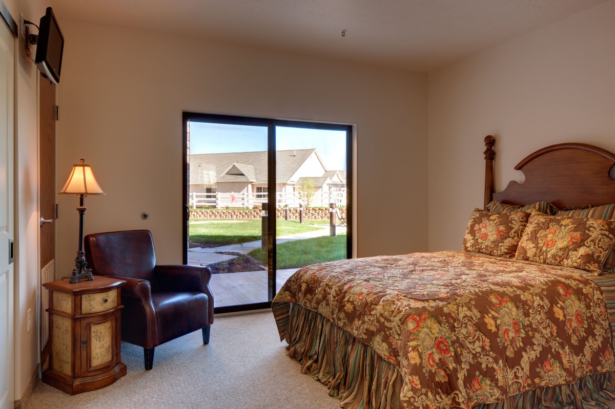 A cozy bedroom with a large bed, armchair, and natural light streaming through a sliding glass door.