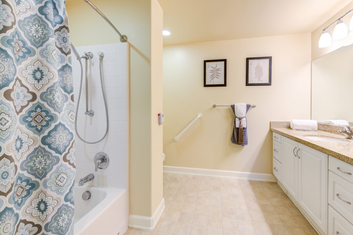 A modern bathroom featuring a shower with a patterned curtain, neatly arranged towels, and framed artwork on the wall.
