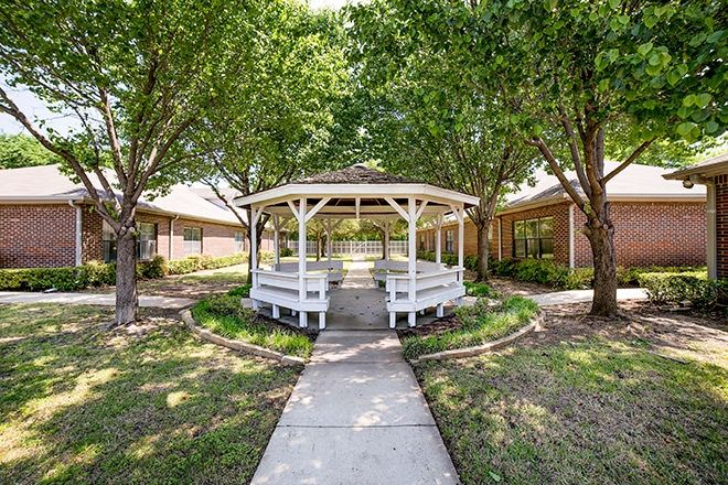 A charming white gazebo surrounded by trees and greenery, with a pathway leading to it.