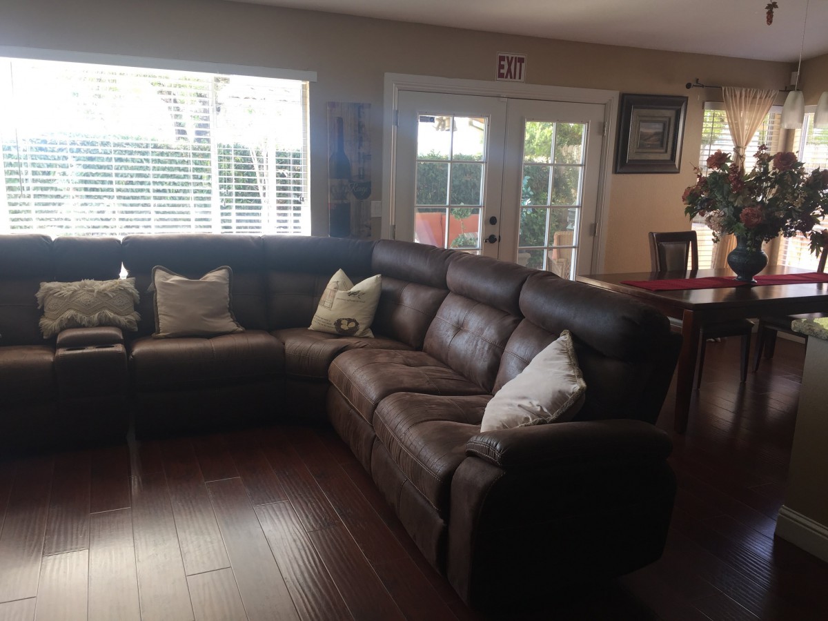 A cozy living room featuring a large sectional sofa with pillows and ample natural light coming through the windows.