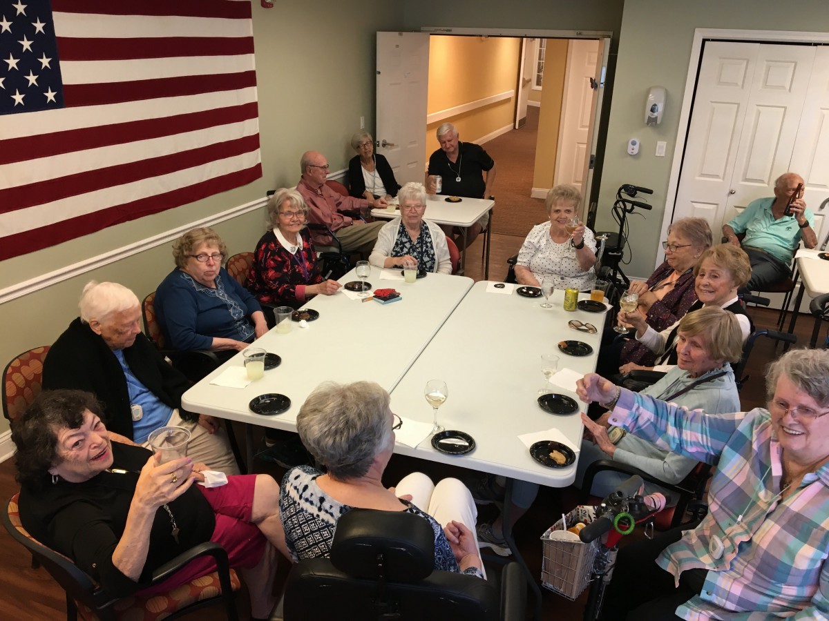 A group of seniors gathered around tables for a meeting or social event indoors.
