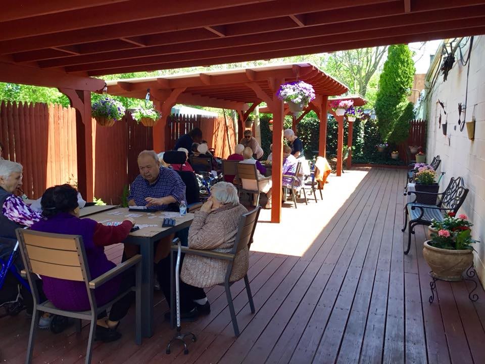 A group of people sitting and socializing on a sunny outdoor patio with wooden decking.