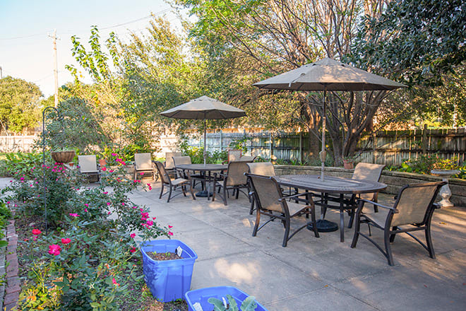 An inviting outdoor patio area with tables, chairs, and umbrellas surrounded by lush greenery.