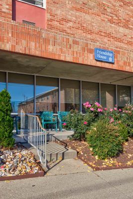 The entrance to an office building with glass windows, a ramp, and surrounding shrubbery.