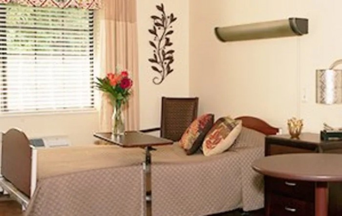 A cozy room featuring a neatly made bed, decorative pillows, and a vase of flowers by the window.