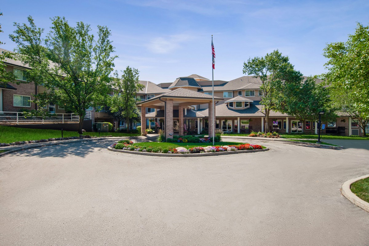 A well-maintained building entrance with surrounding trees and a flagpole at the center of the driveway.