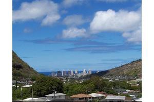 A scenic view of the city skyline nestled between two mountains with an ocean in the distance and fluffy clouds in the sky.