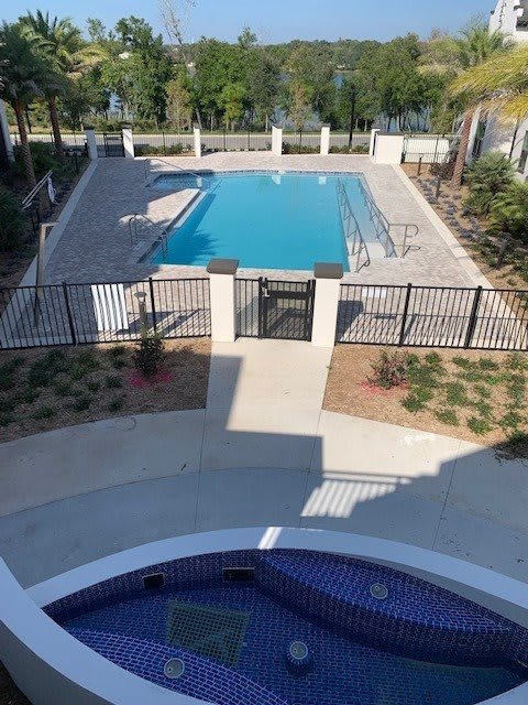 A fenced outdoor swimming pool area with surrounding landscaping on a sunny day.