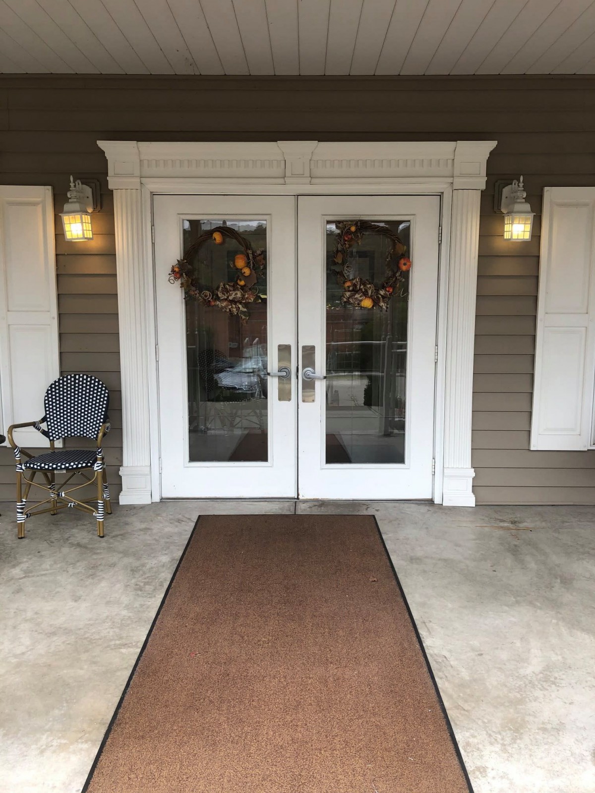 A welcoming porch with double doors adorned by wreaths and a cozy chair.