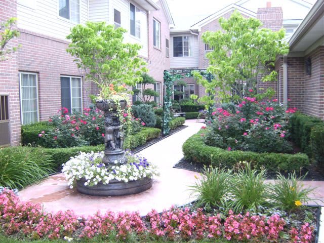 A beautifully landscaped garden with a walkway, surrounded by flowers and greenery, featuring a central fountain.