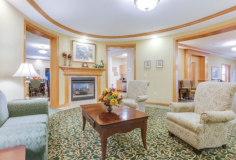 A cozy, traditionally decorated living room featuring a fireplace, armchairs, and a carpet with intricate patterns.