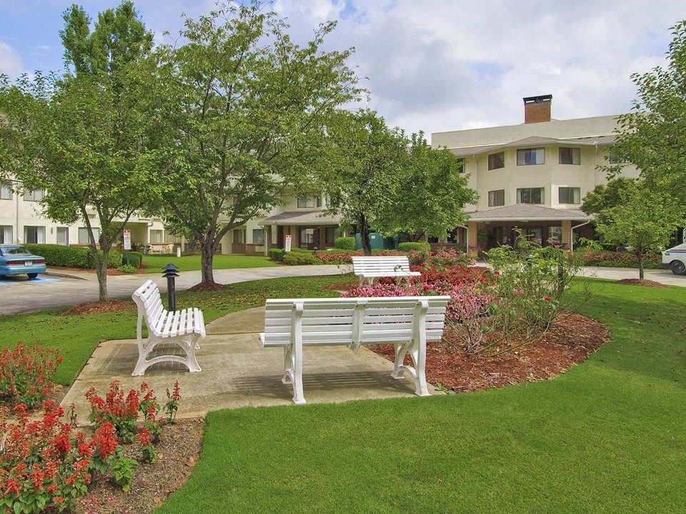 A scenic outdoor garden with benches surrounded by lush landscaping and a nearby building.