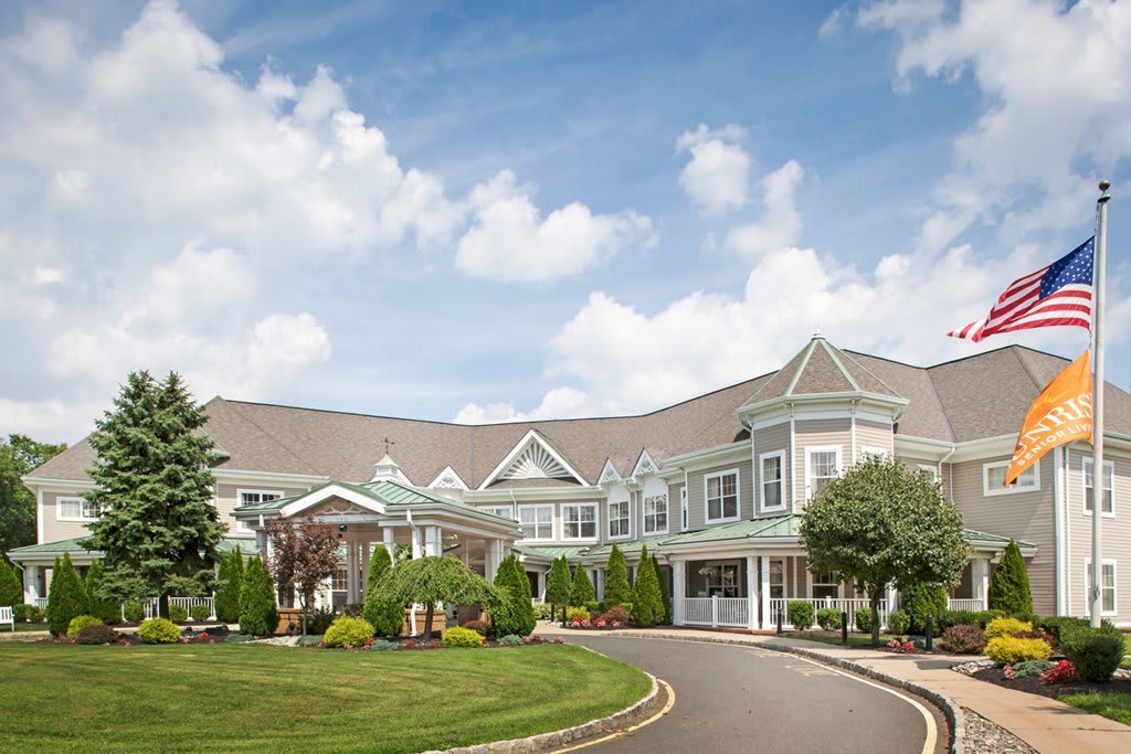 A beautiful residential building with a landscaped garden and driveway under a partly cloudy sky.