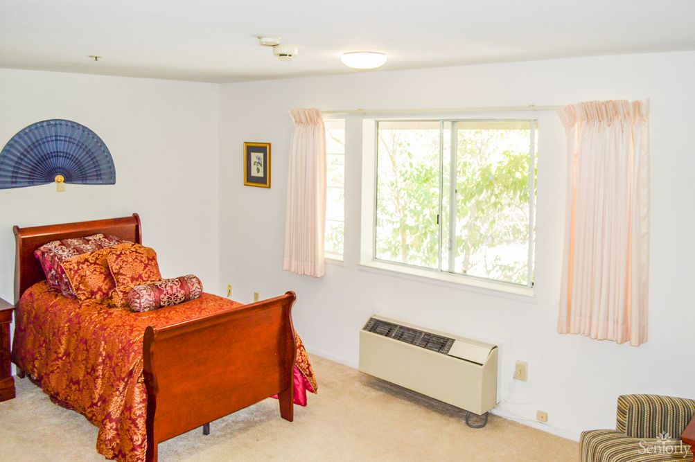 A cozy bedroom with a wooden bed and a large window letting in natural light.