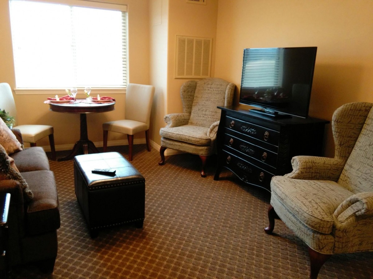 A cozy living room with a TV, chairs, a small table, and a window.