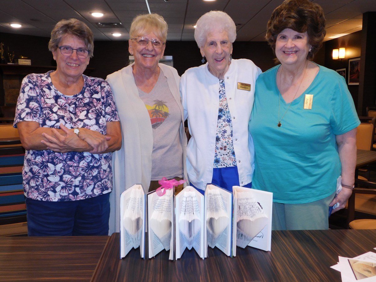 A group of women smiling together at an indoor gathering with books displayed in front of them.