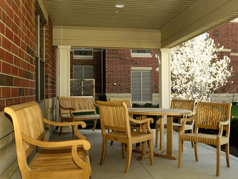 A cozy outdoor porch with wooden chairs and a table, set against a brick building.