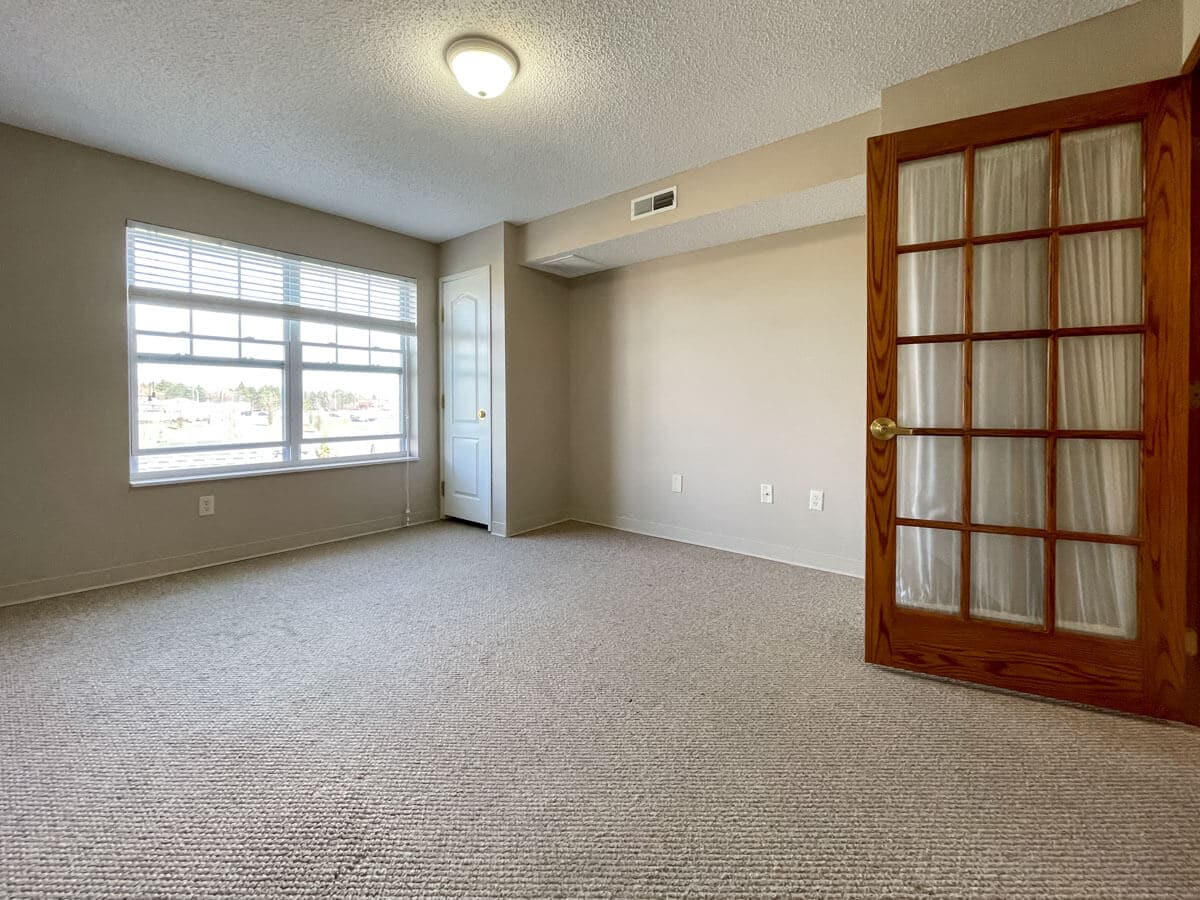 A bright, empty room with carpet flooring and French doors.