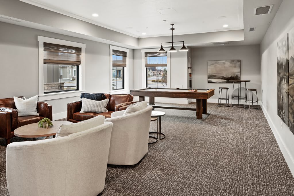 A modern game room featuring a pool table, comfortable seating, and large windows providing ample natural light.