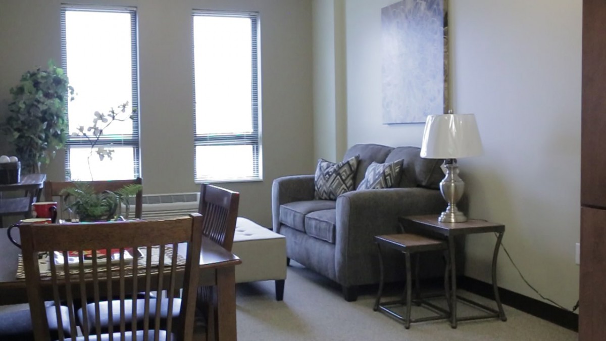 A cozy living room with a sofa, lamp, and tables near a window.