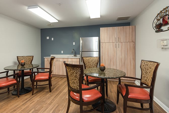 A modern dining area with round tables and upholstered chairs, featuring a refrigerator and wood flooring.