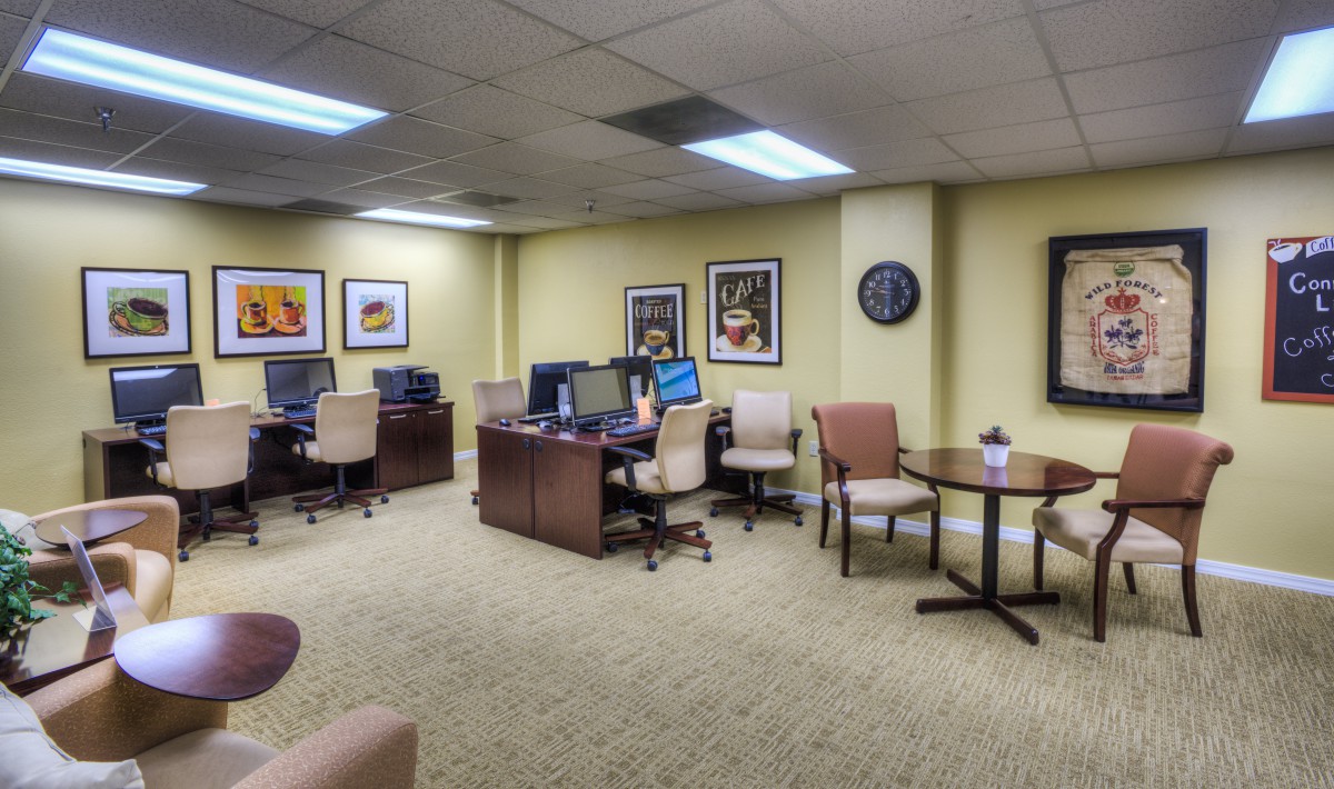 A spacious office area with multiple workstations, featuring computers on desks, comfortable chairs, and artwork on the walls.