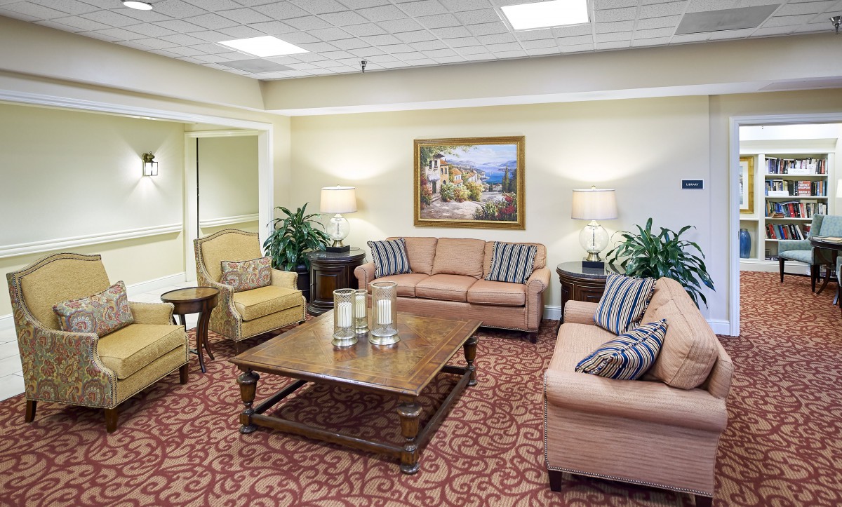A cozy living room with sofas, armchairs, and a coffee table, decorated with indoor plants and framed artwork.